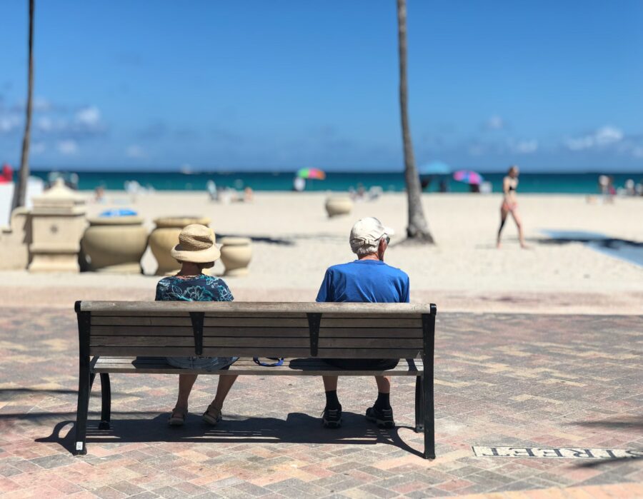 A retired couple sitting on a bench at the beach.
