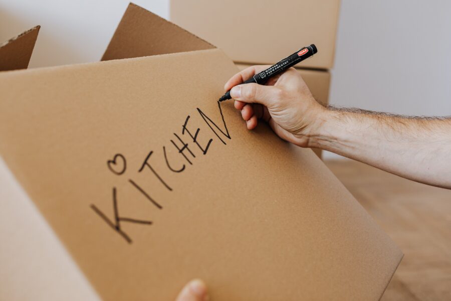 A person using a marker to write the word kitchen on a moving box